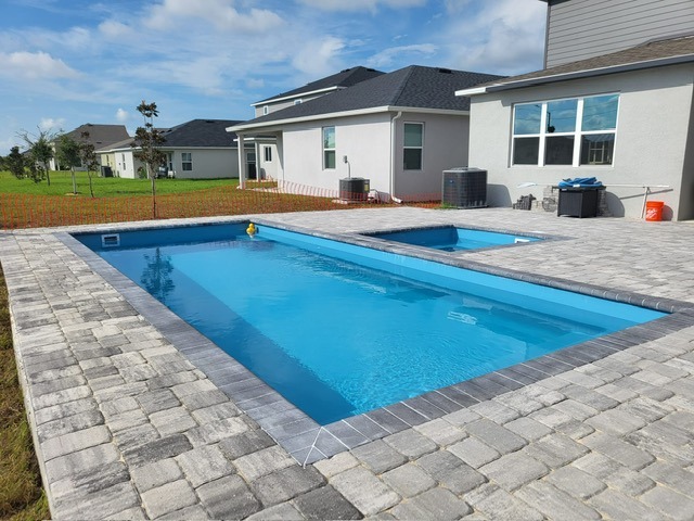 Modern outdoor area featuring a newly constructed swimming pool, surrounded by pavers, with a rubber duck floating on the water.